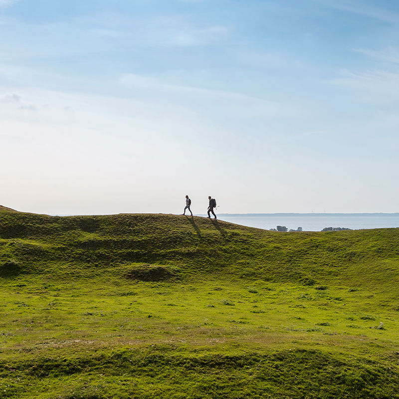 Par vandrar på grön kulle med havet i bakgrunden