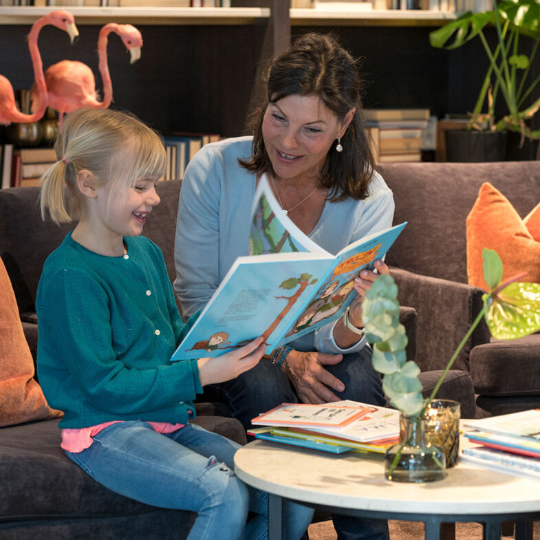 Kvinna och flicka läser barnbok i lounge.